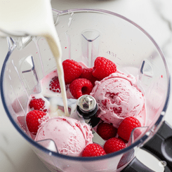 A blender containing a raspberry milkshake mixture with ice cream and whole raspberries, prepared for blending.