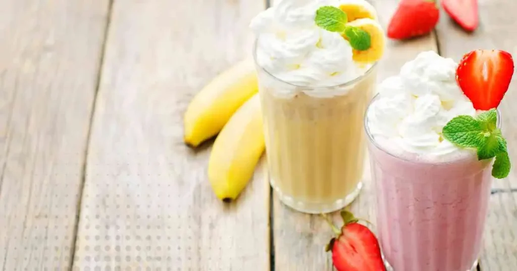 Two refreshing Strawberry Banana Milkshakes with whipped cream and strawberries, set on a wooden table.