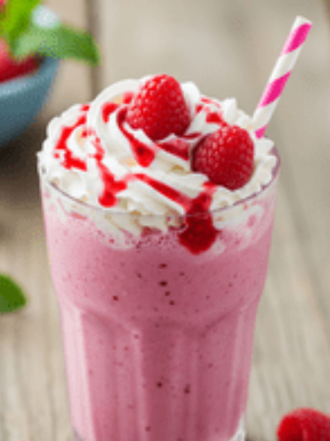 A vibrant raspberry milkshake with a swirl of whipped cream and garnished with strawberries on top.