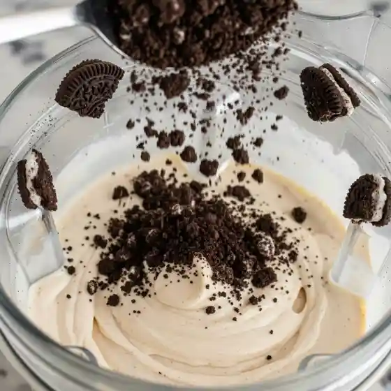 Crushed cookies fall into a blender filled with creamy mixture, surrounded by cookie halves. The scene feels indulgent and festive, reminiscent of the fun and bold vibe often associated with Edgar haircuts for men.