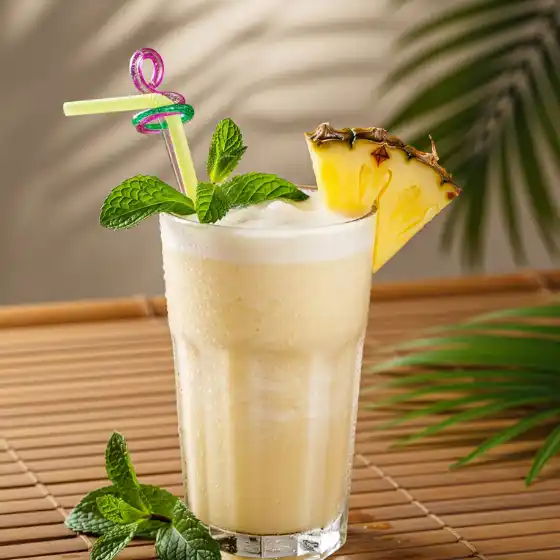 A frothy tropical Pineapple Milkshake Recipe with a pineapple slice and mint leaves, served in a glass with a colorful straw on a bamboo mat, evoking a fresh, summery vibe.