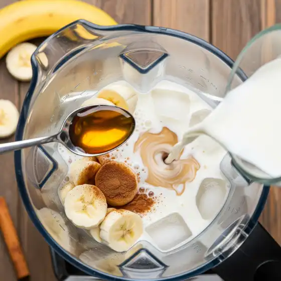 Ingredients for a Banana Milkshake Recipe: sliced bananas, honey, cinnamon, and milk are added to a blender with ice cubes.