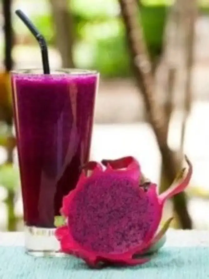 A vibrant pink smoothie in a glass with a straw, alongside a sliced dragon fruit, featuring its bright pink skin and dotted flesh. Perfect representation of a Dragon Fruit Shake Recipe.