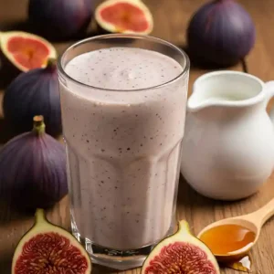 A creamy Fig milkshake in a tall glass on a wooden table, surrounded by fresh figs, a small white jug, and a spoonful of honey.