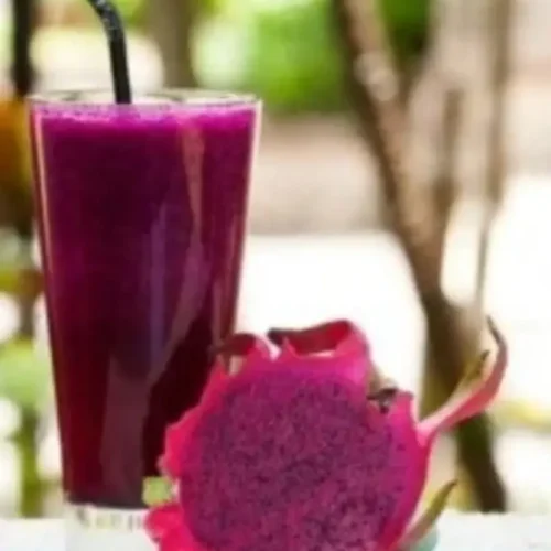 A vibrant pink smoothie in a glass with a straw, alongside a sliced dragon fruit, featuring its bright pink skin and dotted flesh. Perfect representation of a Dragon Fruit Shake Recipe.